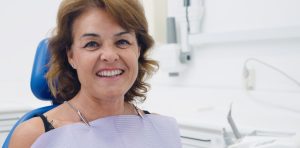 Una signora over 50 che sorride seduta sulla poltrona dello studio dentistico